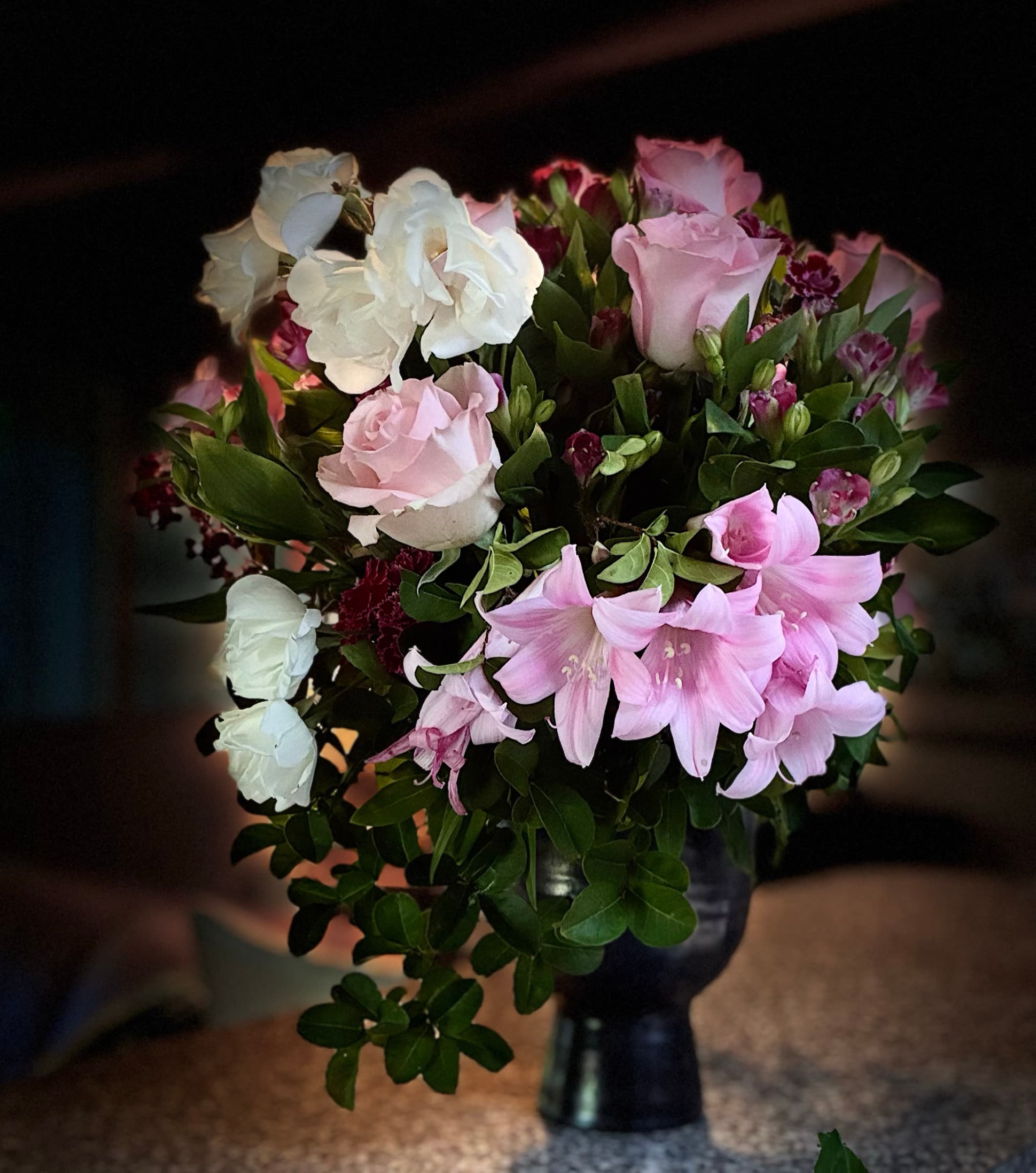 Blush lilies and white roses in a dark pedestal vase