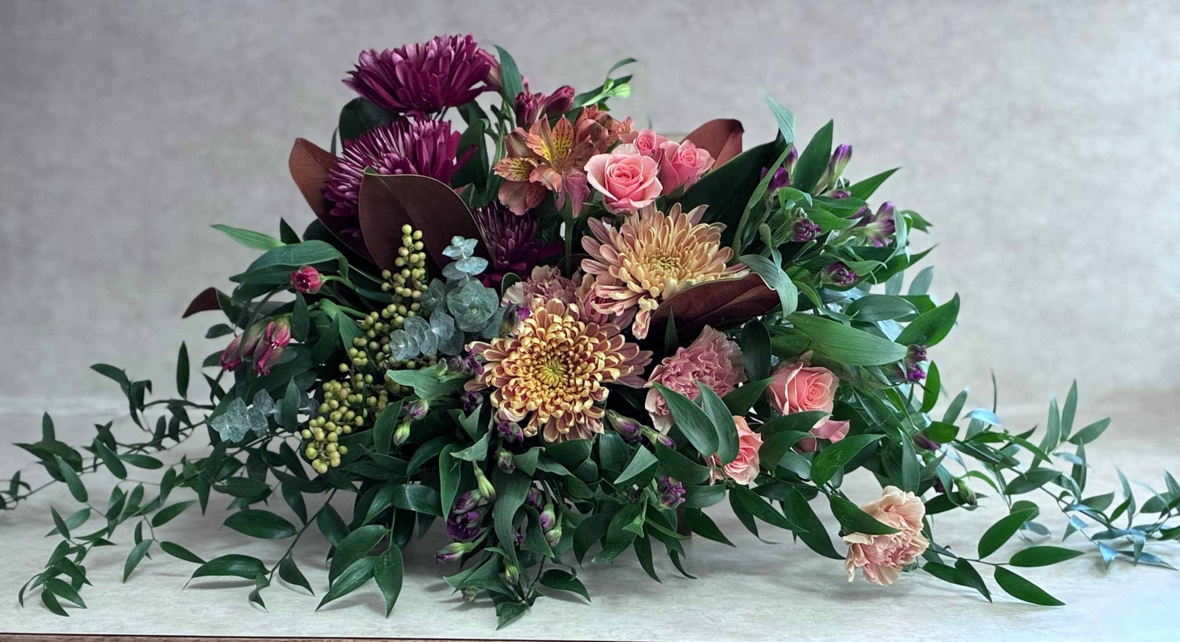 Low autumn centerpiece of mums, roses and trailing greens